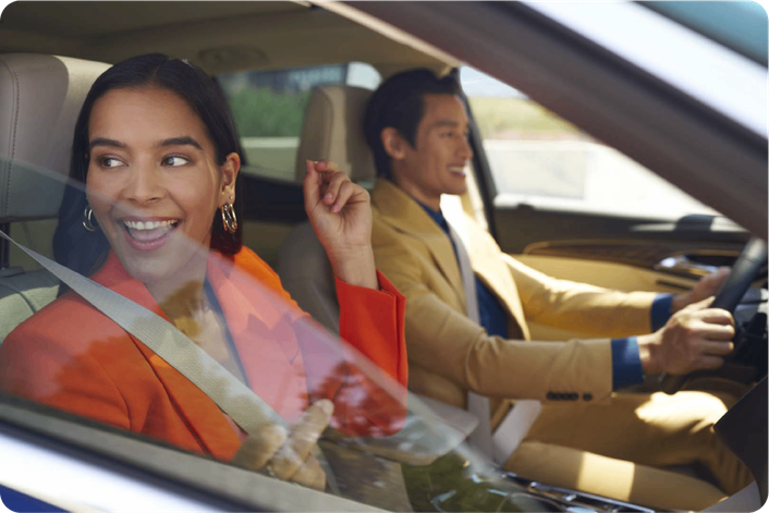 Pareja disfrutando un viaje en auto Chevrolet, mujer en el asiento delantero y conductor sonriendo.