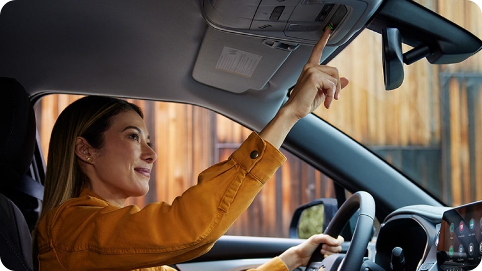 Mujer manejando un Chevrolet y activando el sistema OnStar desde el techo del vehículo.
